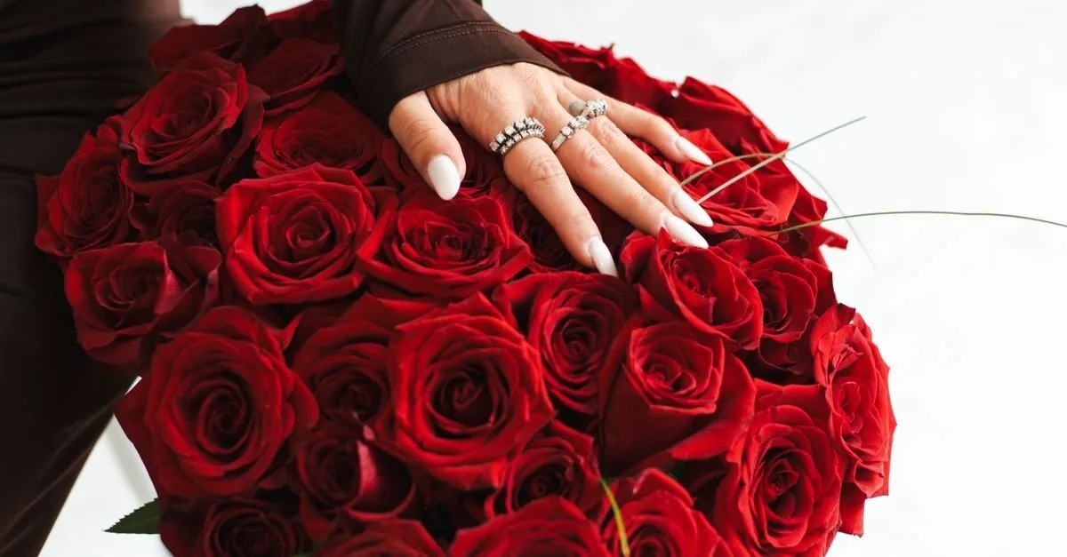 Large red rose bouquet with a hand resting over the flowers